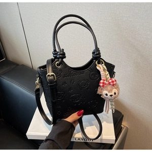 Detail of black embossed bear bucket bag with plush charm on a geometric display