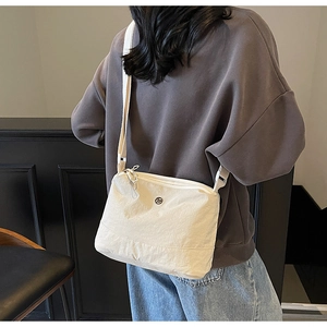 Close-up of lightweight off-white canvas crossbody bag with adjustable strap on a person