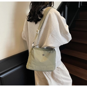 Green lightweight nylon crossbody bag shown from the side on a casual lifestyle model