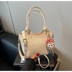 Detailed view of the creamy white bucket bag with cartoon animal embossing and bear charm