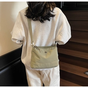 Close-up of sage green canvas crossbody bag with metal logo and adjustable strap
