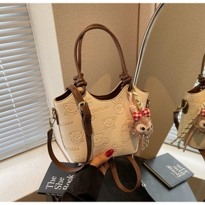 Detail of cream bucket bag with cartoon animal embossing and plush charm accessory