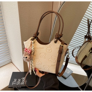 Detail of cream bucket bag with cartoon bear embossing and plush charm hanging on side