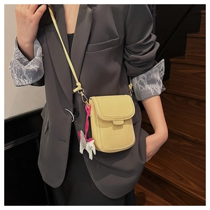 Gros plan d'un sac bandoulière jaune en cuir grainé avec breloque cheval sur blazer