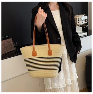Model showcasing a large striped straw tote bag with brown leather handles in a chic setting