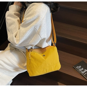 Detail of bright yellow nylon crossbody bag with adjustable strap and metal logo