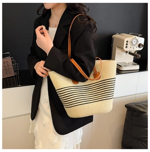 Straw tote bag with black stripes and brown leather handles on a lifestyle model