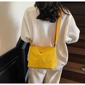 Detail of a bright yellow nylon crossbody bag with adjustable strap worn by a model