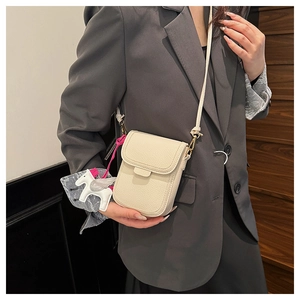 Détail du sac de téléphone crème avec texture litchi et breloque pégase sur blazer gris