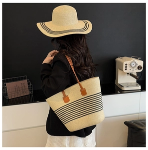 Detailed view of woven straw tote bag and sun hat with black stripes and brown straps