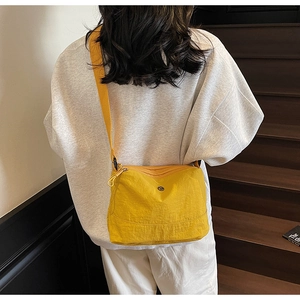 Detail view of the yellow canvas crossbody bag featuring dual zippers and adjustable strap