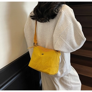 Detail of bright yellow nylon crossbody bag with circular metal logo on model