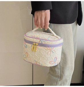 Detailansicht goldener Reißverschlüsse und Stickereien auf cremefarbener Kosmetiktasche