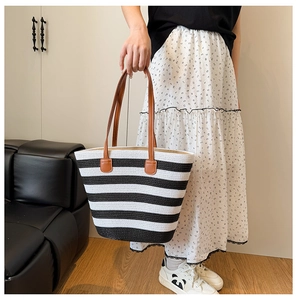 Macro detail of black and white striped straw tote bag showing brown leather handles