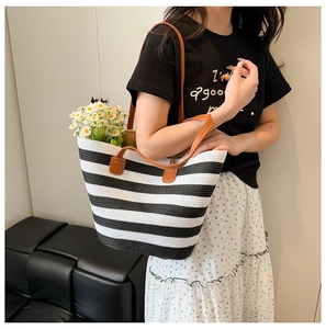Detail of hand-woven straw tote with black and white stripes and brown leather handles
