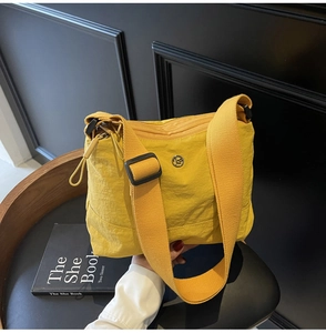 Close-up of bright yellow nylon crossbody bag with wide strap and round metal logo