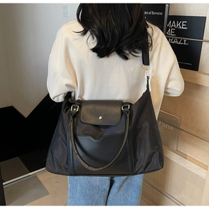 Détail d'un grand sac cabas noir avec poignées en cuir et large bandoulière en textile