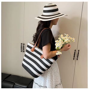 Close-up of a striped straw tote bag with brown leather handles and summer hat detail