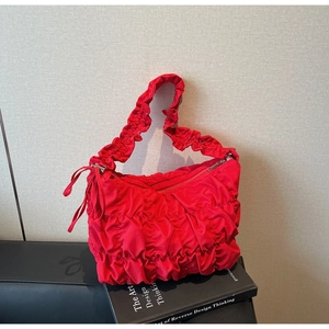 Close-up of bright red pleated handbag featuring ruffled strap and silver zipper detail