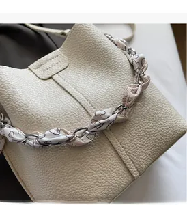 Close-up of beige lychee leather bucket bag with silk scarf and silver chain handle