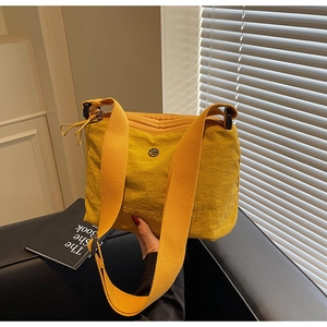 Detail of yellow nylon crossbody bag featuring a circular logo and durable wide strap
