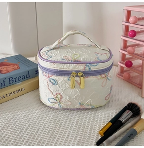 Detail der weißen gesteppten Kosmetiktasche mit bunter Blumenstickerei und Goldzipper
