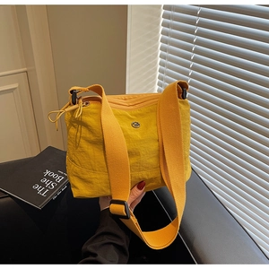 Detail of yellow nylon crossbody bag with wide shoulder strap and metal logo accent
