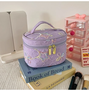 Detail der lila gesteppten Kosmetiktasche mit bunten Stern- und Schmetterlingsstickereien