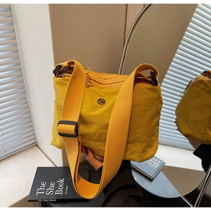 Detailed mirror view of bright yellow nylon crossbody bag with wide strap and metal logo