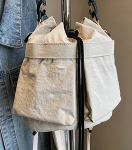 Detailweergave van beige canvas rugzak met trekkoord, zijzakken en contraststiksels