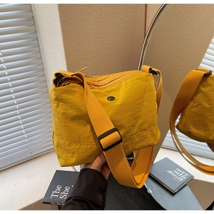Detail of yellow nylon crossbody bag featuring wide strap and circular metal logo plaque