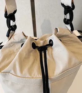 Detail van de trekkoordsluiting en de zwarte clip op de beige canvas bucket bag voor dames