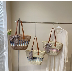 Three woven straw tote bags with leather handles and decorative silk scarves in a sunny room