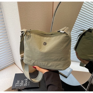 Detail of sage green canvas crossbody bag featuring adjustable strap and round metal logo