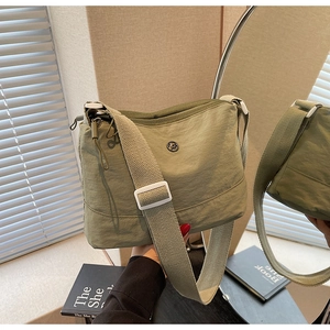 Detail of sage green nylon crossbody bag featuring adjustable strap and circular logo