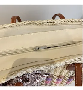Close-up of smooth top zipper closure and beige fabric lining on woven straw tote bag