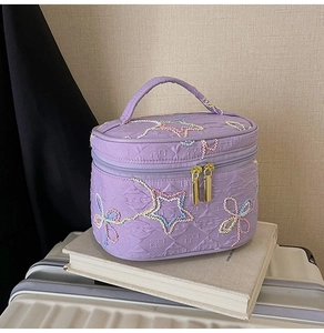 Detail der lila gesteppten Kosmetiktasche mit Sternstickerei und Doppelreißverschluss