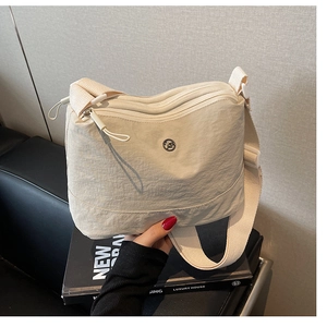 Detail of beige canvas crossbody bag featuring double zippers and a round metal logo