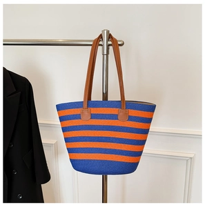 Detail of blue and orange striped straw tote bag with brown leather handles on a hanger