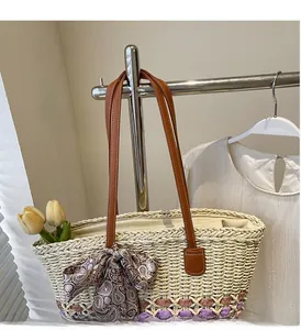 Detail of straw woven tote bag featuring purple base and brown leather handles with ribbon