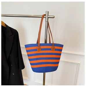 Detail of blue and orange striped straw tote bag with brown leather handles on hanger