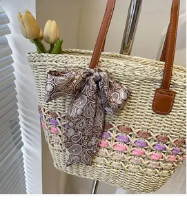 Detail of woven straw tote bag featuring brown leather handles and paisley silk scarf bow