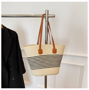 Close-up of a striped straw tote bag with brown leather handles hanging on a silver rack