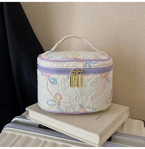 Details von Blumenstickerei und Goldreißverschluss auf cremefarbener Kulturtasche