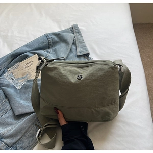 Detail of army green canvas crossbody bag with adjustable strap on white bedding