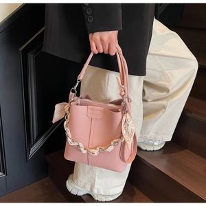 Detailed shot of a pink pebbled leather bucket bag with silk scarf and gold chain