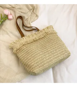 Detail of beige straw tote bag featuring decorative fringe trim and brown leather handles