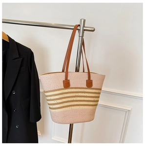 Detail of pink and beige striped woven straw tote bag with brown leather handles