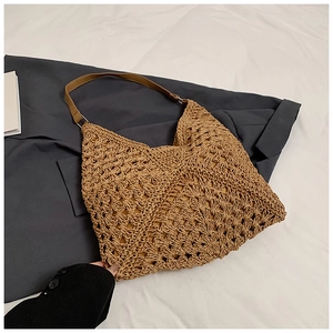 Detail of hollow crochet straw tote bag with brown leather strap on neutral fabric