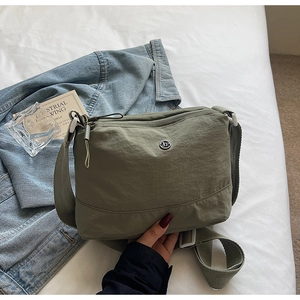 Detailed shot of an olive green canvas crossbody bag with a wide strap and metal logo